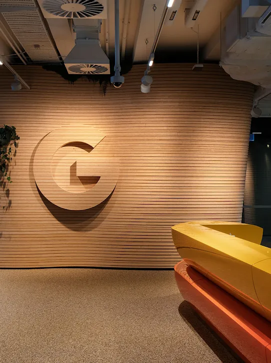 Uma recepção com o logotipo do Google, uma mesa e plantas diversas.