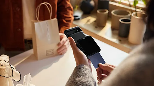 A customer inserting a credit card into a mobile card reader attached to a smartphone to complete a purchase in a shop.