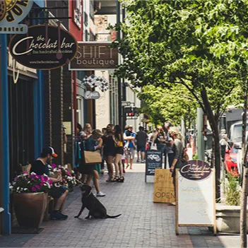 A man in a baseball cap sits on the edge of a large planter filled with flowers on a busy city sidewalk