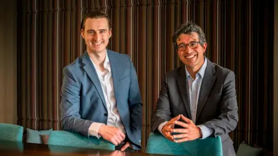 Two men stood behind the chairs and posing for picture.