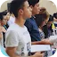 A diverse group of young men and women standing together, focused on reading from small handheld books or bibles.