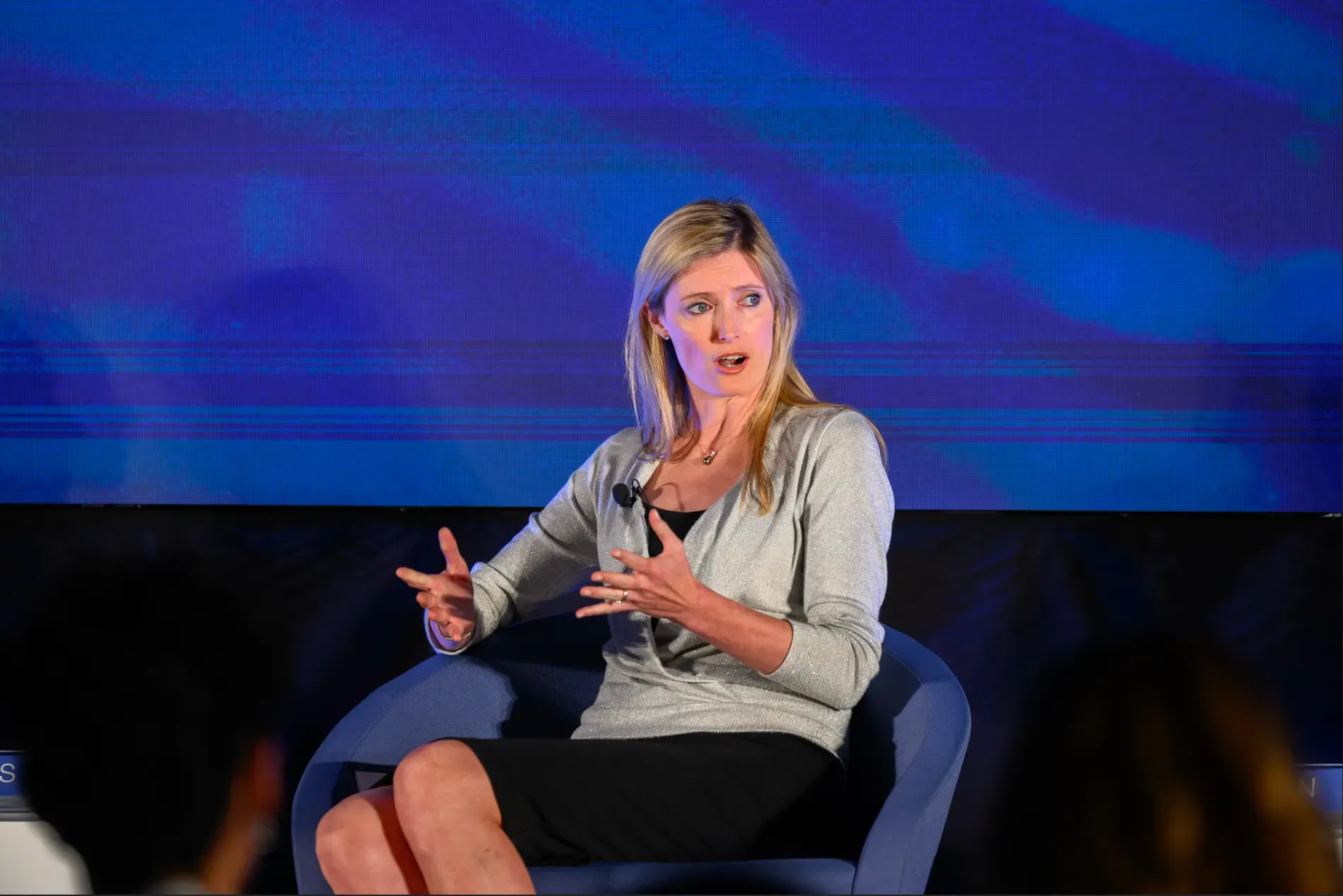 Alexandra Reeve Givens, CEO of the Center for Democracy and Technology, speaking on a panel at the World Economic Forum AI Governance Summit in San Francisco. She is gesturing during her talk while seated in a blue chair against a large blue digital screen.