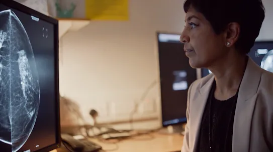 A healthcare professional reviewing a mammogram on a computer monitor. 