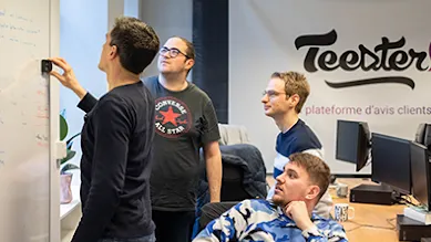 Four men are writing on a whiteboard in front of the Teester company sign.