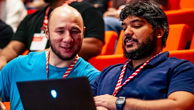 Two audience members are engrossed in a laptop.