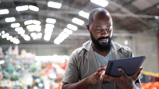 A professional man uses a tablet while working in a warehouse.