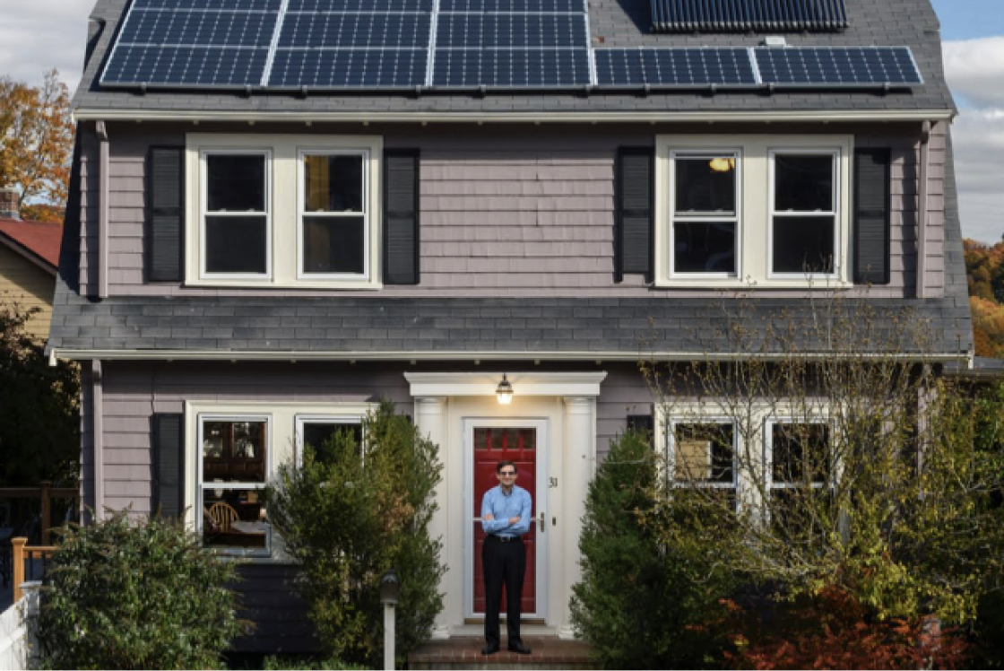 Hombre de pie frente a una casa pintoresca que tiene instalados paneles solares en la azotea.