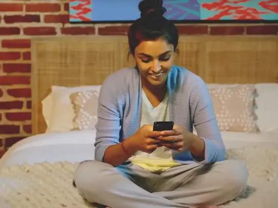 Woman sitting on bed with Android phone