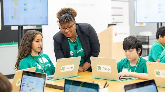 An instructor helps a girl and boy on laptops 