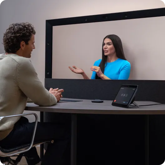 A person seated at a desk participating in a 3D video meeting with a colleague doing hand gestures.