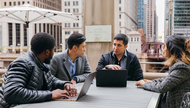 3 men and a woman sitting around a table, discussing.