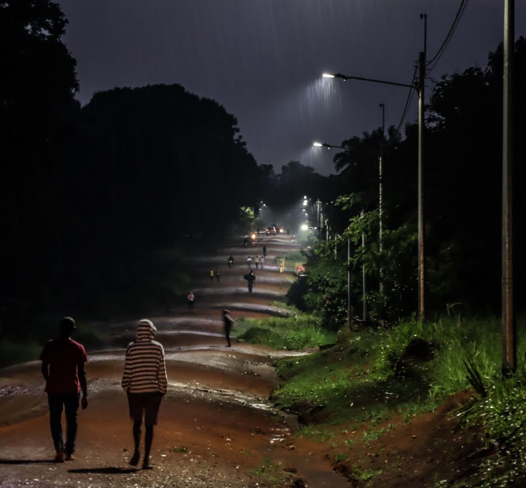 People walking down a road at night with streetlamps lining the road to improve visibility, accessibility