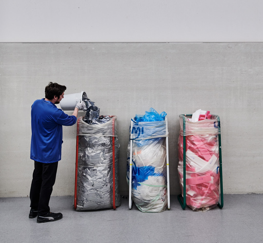 A person wearing a cobalt blue shirt, black pants and black shoes pouring metallic packaging materials into a bag