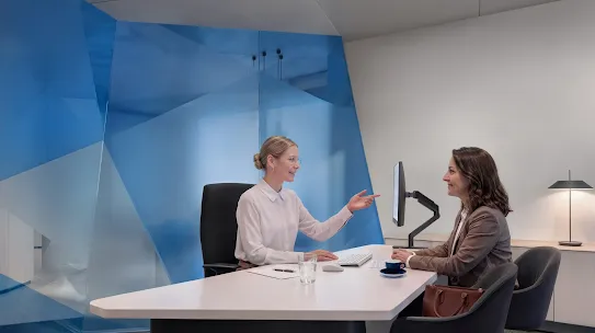 A female Deutsche Bank customer service agent talks to a woman while they both are sitting in a corporate office.