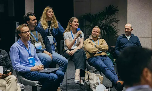 A group of people is sitting and a girl amongst them telling something.