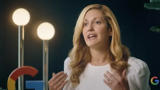 A professional video still of Kate Brandt, Google’s Chief Sustainability Officer, speaking during an interview. She is wearing a white top against a dark background with blurred globe-shaped lights and a partial Google "G" logo in the frame.