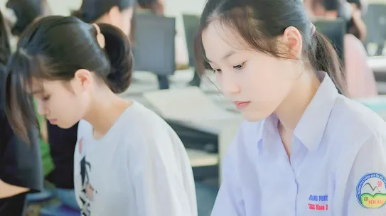 A focused young woman in a student uniform working at a computer in a classroom, illustrating the Bamboo Builders and ScamWISE initiative to educate people on digital literacy.