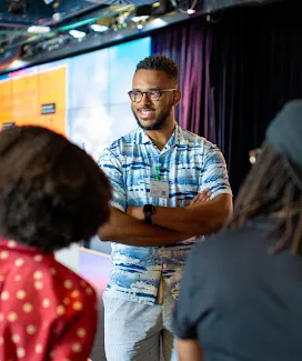 A man wearing black shirt discussing with team, smiling.