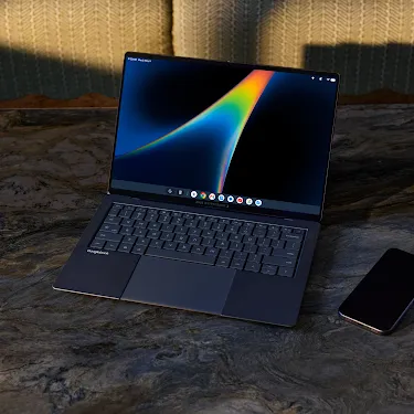 Googlebook open on a marble table with a phone nearby.