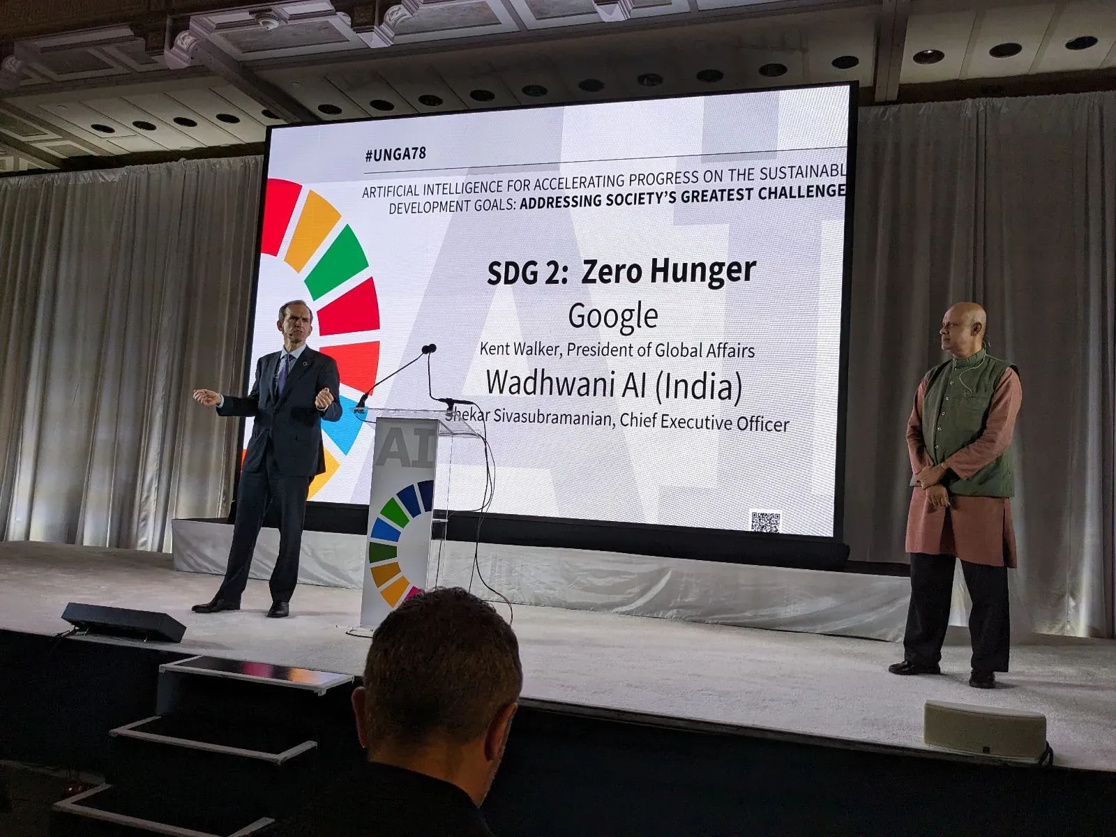 Google President of Global Affairs Kent Walker and Wadhwani AI CEO Shekar Sivasubramanian on stage at UNGA78. A large screen behind them displays "SDG 2: Zero Hunger" and "Artificial Intelligence for Accelerating Progress on the Sustainable Development Goals."