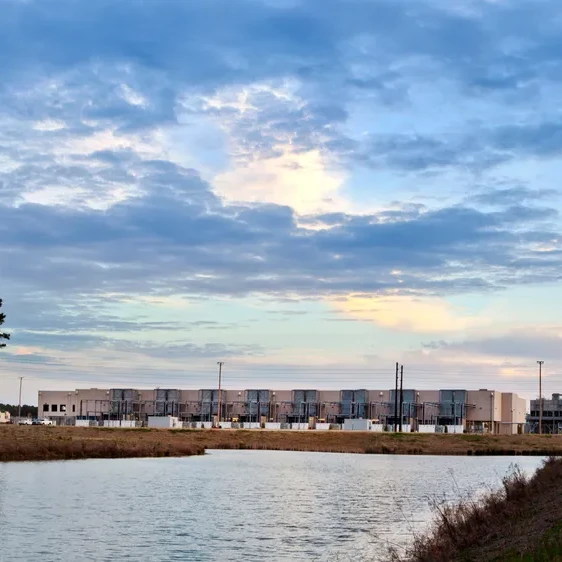 Industrial facility behind pond, pine trees.