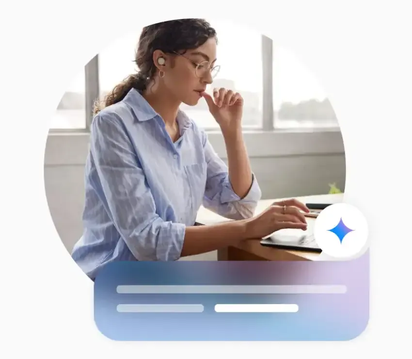 A person in business casual attire has earbuds on looking at a laptop at a wooden table. The Google Gemini icon and prompt interface is at the lower right corner.
