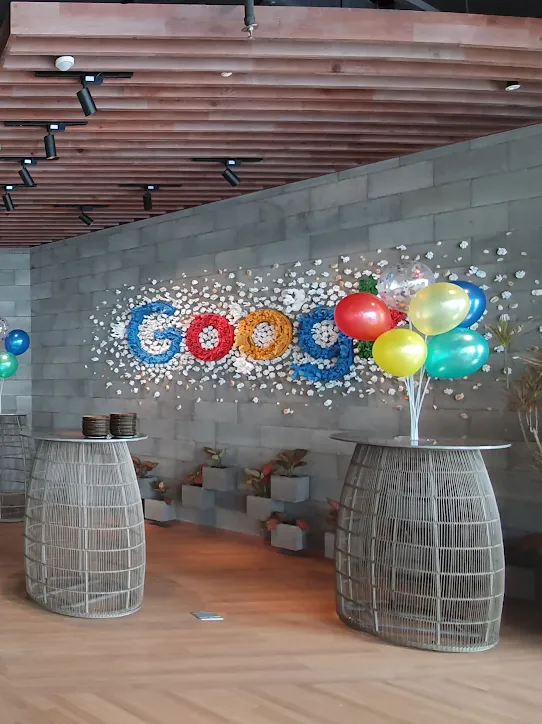 Kutlama için süslenmiş bir Google ofis alanı. Metal iskeletli masaların üzerinde renkli balonlar duruyor ve tavandan büyük, ipek şemsiyeler sarkıyor.