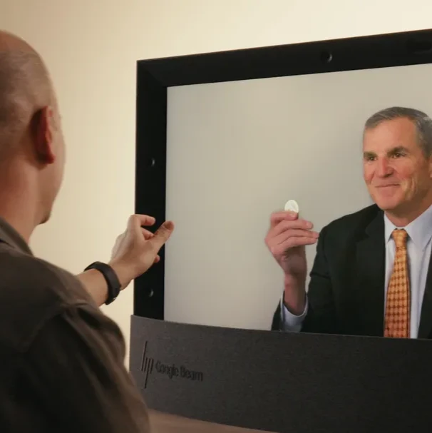 The USO CEO is holding the coin up to the camera, and the depth makes appear as if it is being presented directly across the desk to the local viewer
