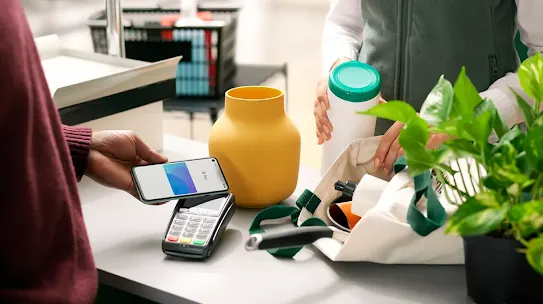 A person using a smartphone to make a Tap and Pay contactless payment at the checkout counter.