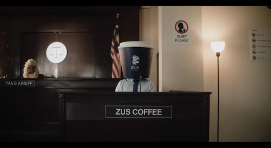 The video thumbnail depicts a humorous courtroom setting with actors dressed as a judge and lawyers, reflecting the video's theme of ZUS Coffee being put on "trial" to determine if it is a "Buatan Malaysia" (Made in Malaysia) brand.
