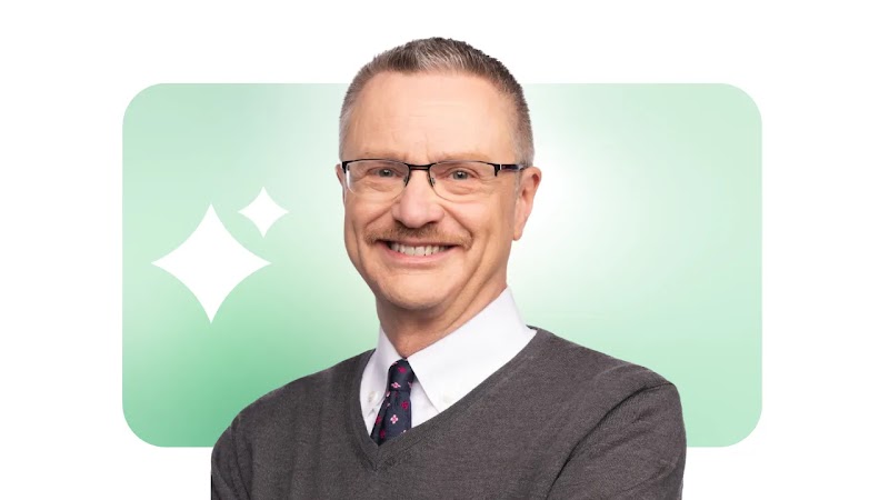 Portrait du professeur et auteur Jim Lecinski, qui apparaît souriant. Il a les cheveux courts, la peau et les yeux clairs, et il porte des lunettes, un pull, une chemise et une cravate. Le logo de l'IA de Google, en forme d'étincelle, apparaît derrière lui.
