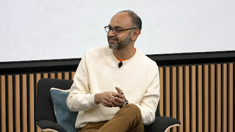 Harikesh Nair, senior director of data science and engineering at Google, sits in a chair while speaking on a panel. Nair has medium skin, short dark hair and beard, and wears a cream pullover sweater.
