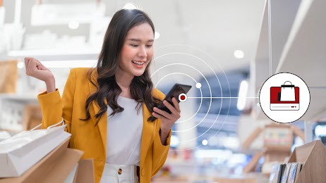 A woman holding multiple shopping bags uses her phone in-store, representing how data-driven Online-Merge-Offline (OMO) marketing and omnichannel retail strategies can help retailers like Muji maximise sales