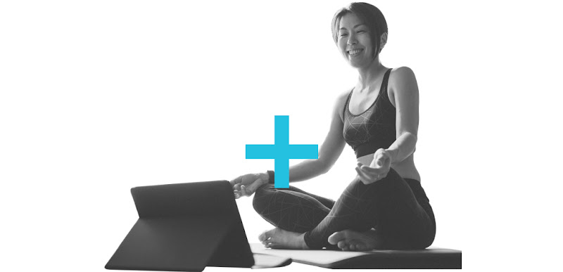A Singaporean woman sitting on a yoga mat and smiling at her tablet