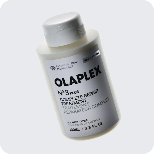 A small, clear bottle of yellow Olaplex hair oil sits on a wooden surface, catching the light in a warm, indoor setting. A stat callout reads “+93% Search lift.”