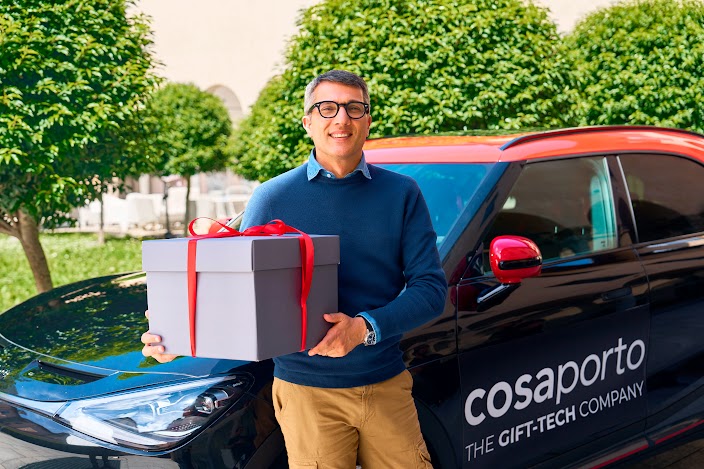 Andrea Magra, Country Manager per il Regno Unito di Cosaporto, in piedi accanto a un'auto con il marchio dell'azienda, con in mano un regalo.