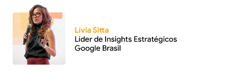 Foto de Lívia Sitta, Líder de Insights Estratégicos do Google Brasil. Ela é uma mulher branca, com cabelos longos cacheados, usa óculos e blusa preta. Ela segura um microfone e olha em direção a uma audiência.