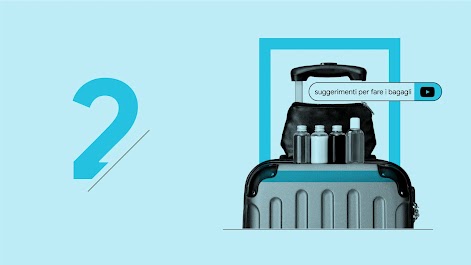 Il termine di ricerca "suggerimenti per fare i bagagli" appare in una barra di ricerca di YouTube sopra un kit per l'igiene personale appoggiato su un trolley.