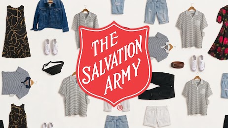 The red and white Salvation Army shield emblem appears against a white background with gray, black, red, and white articles of clothing, including dresses, pants, tops, and shoes, laid flat.