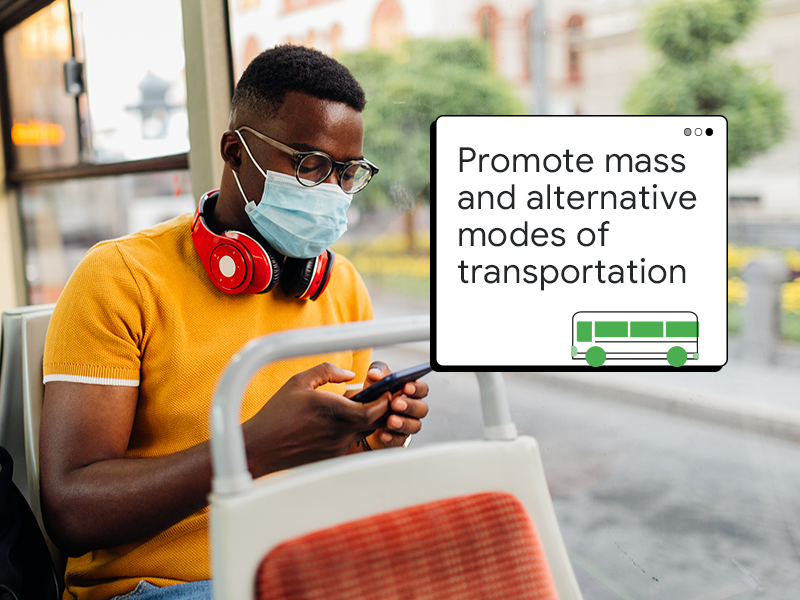 Siyah saçlı ve koyu tenli, gözlüklü, ağzını ve burnunu cerrahi maske ile kapatmış bir adam belediye otobüsünde mobil cihaz kullanıyor. Bir pop-up pencerede "Toplu ve alternatif ulaşım yöntemlerini teşvik edin." yazıyor.