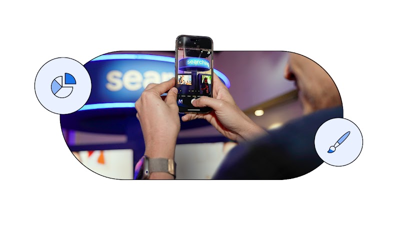 Uma pessoa segura um smartphone e fotografa uma placa luminosa azul com a palavra "searching". Ícones de gráfico de pizza e pincel flutuam ao lado, em tons de azul.