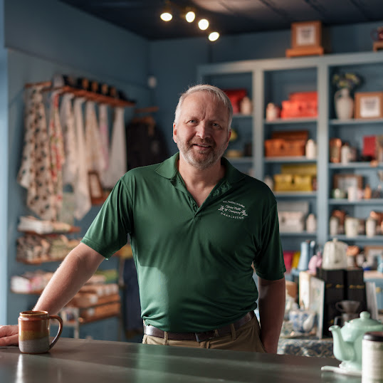 Owner Darren Hartford stands in his tea shop wearing a green Oliver Pluff & Co. shirt