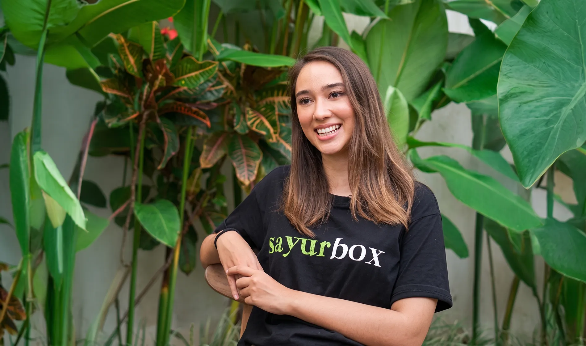 Seorang wanita mengenakan kaos berlogo Sayurbox, tersenyum ke arah kamera