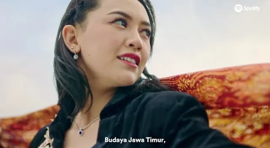 The video thumbnail shows a woman in a black jacket and a necklace, looking up and slightly to the side with a serious expression. She has a white earring and the background appears to feature traditional Indonesian fabric (Batik). The title overlay reads "Suara dari Indonesia: #SpotifySuaraIndonesia" (Voice from Indonesia: #SpotifyVoiceofIndonesia), and the text below her chin says "Budaya Jawa Timur" (East Javanese Culture).
