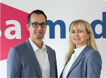 Ein Mann und eine Frau im Anzug vor ihrem Firmenlogo