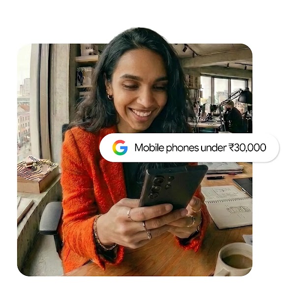 A woman in an orange jacket looking at her smartphone in a bright office, overlaid with a Google search bar reading "Mobile phones under ₹30,000".