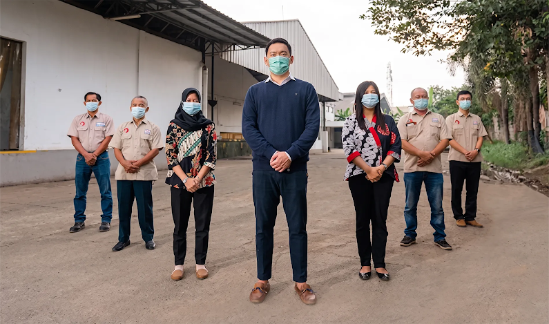 Sebuah tim berdiri bersama di luar fasilitas manufaktur mereka