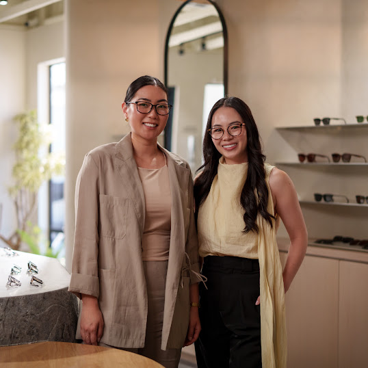Co-founders Florence and Athina stand smiling in their flagship eyewear store, wearing eyeglasses