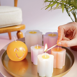 Hema candles arranged on a tray. A hand is lighting the first candle with a match from the right-hand side of the frame.