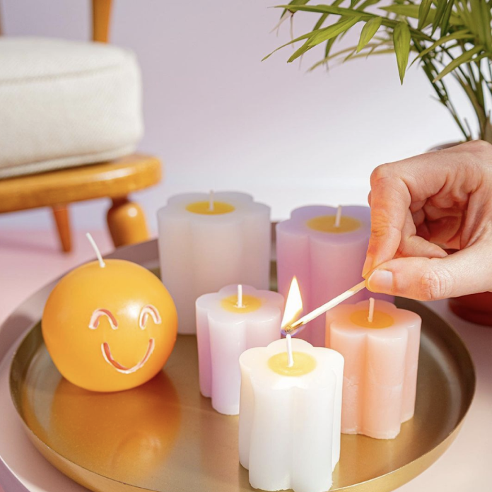 Hema candles arranged on a tray. A hand is lighting the first candle with a match from the right-hand side of the frame.